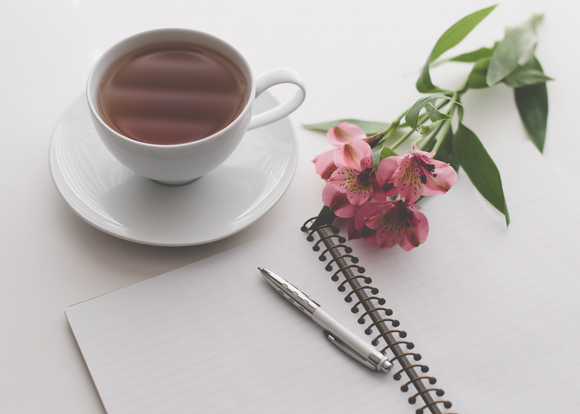 Empty notebook with a pen, pink flowers and a cup of tea